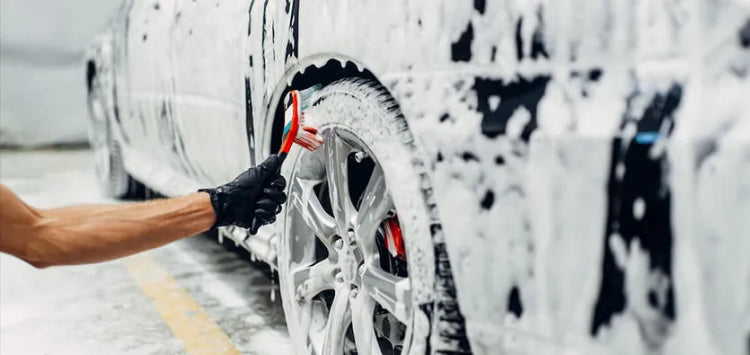 Detailer cleaning car wheels with brush and foam during mobile auto detailing and car care wash.